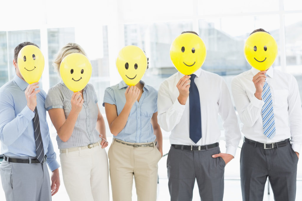 Group of business people holding happy smiles in front of their faces in a bright office