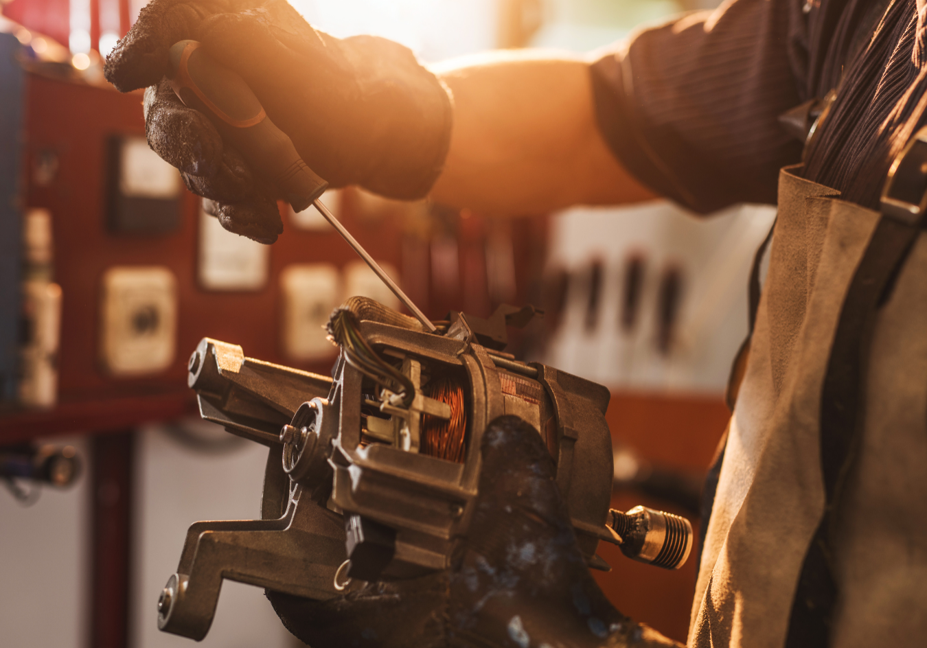 Electric motor engineer repairing a motor with hand tools, dressed in orange safety gear, carefully working on the motor components.