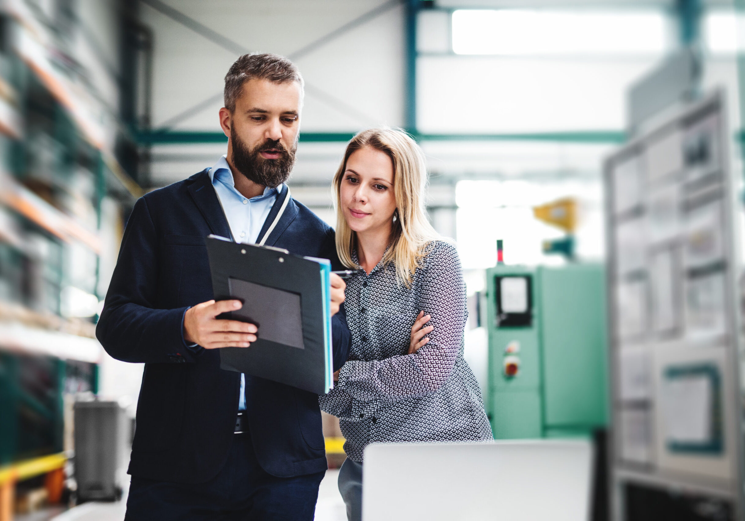 A portrait of a serious mature industrial man and woman engineer with laptop in a factory, working.